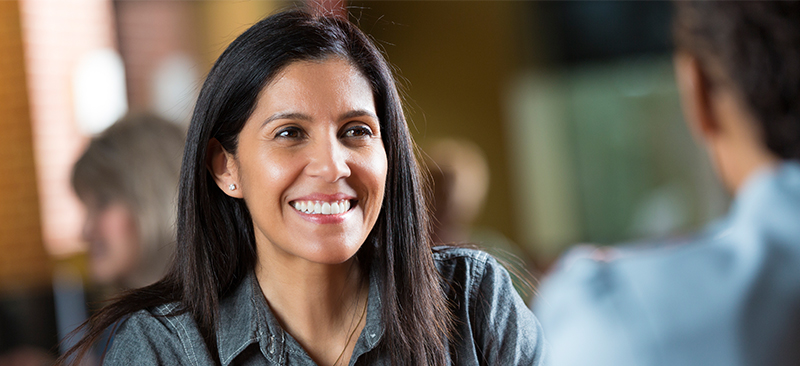 Latinx woman smiling at another person who is out-of-focus