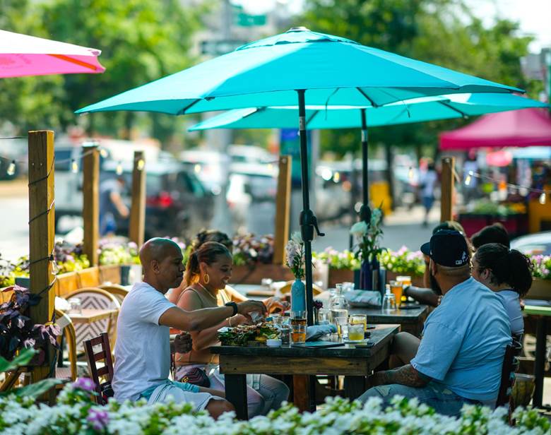 A group of people sitting at a table under a blue umbrella. Description generated by AI