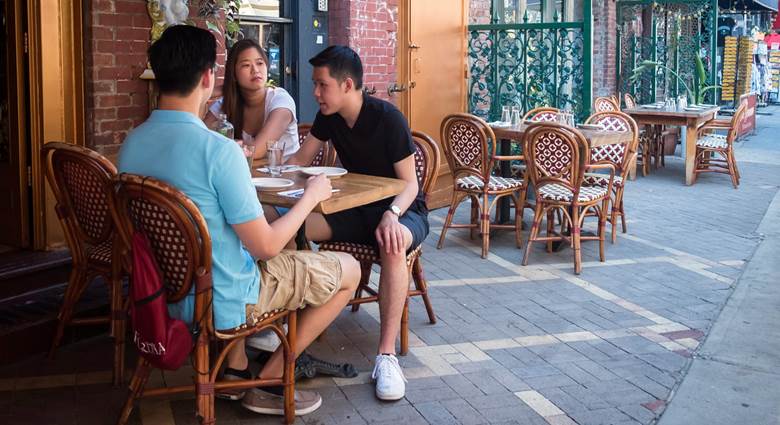 A group of people sitting at a table on a sidewalk. Description generated by AI