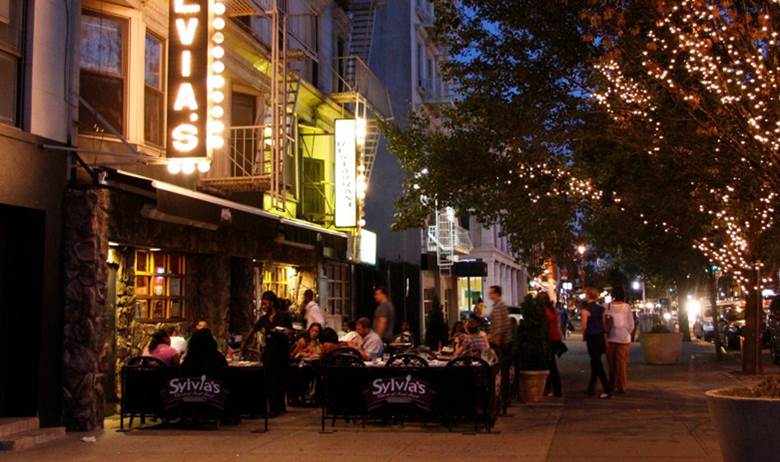 A city street with a restaurant and a tree with lights on it. Description generated by AI