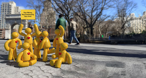 7 Sunshine figures huddled in Washington Square Park with hearts on their chest with a flag that reads 'Your Money, Your Community, Your Vote!''