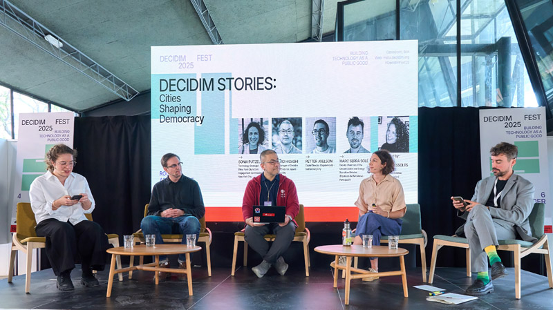 Barcelona: Photo of five people, including Sonia Putzel, the CEC's Technology Strategist, at DecidimFest. They are sitting on a panel in front of a large board that says Decidim Stories: Cities Shaping Democracy