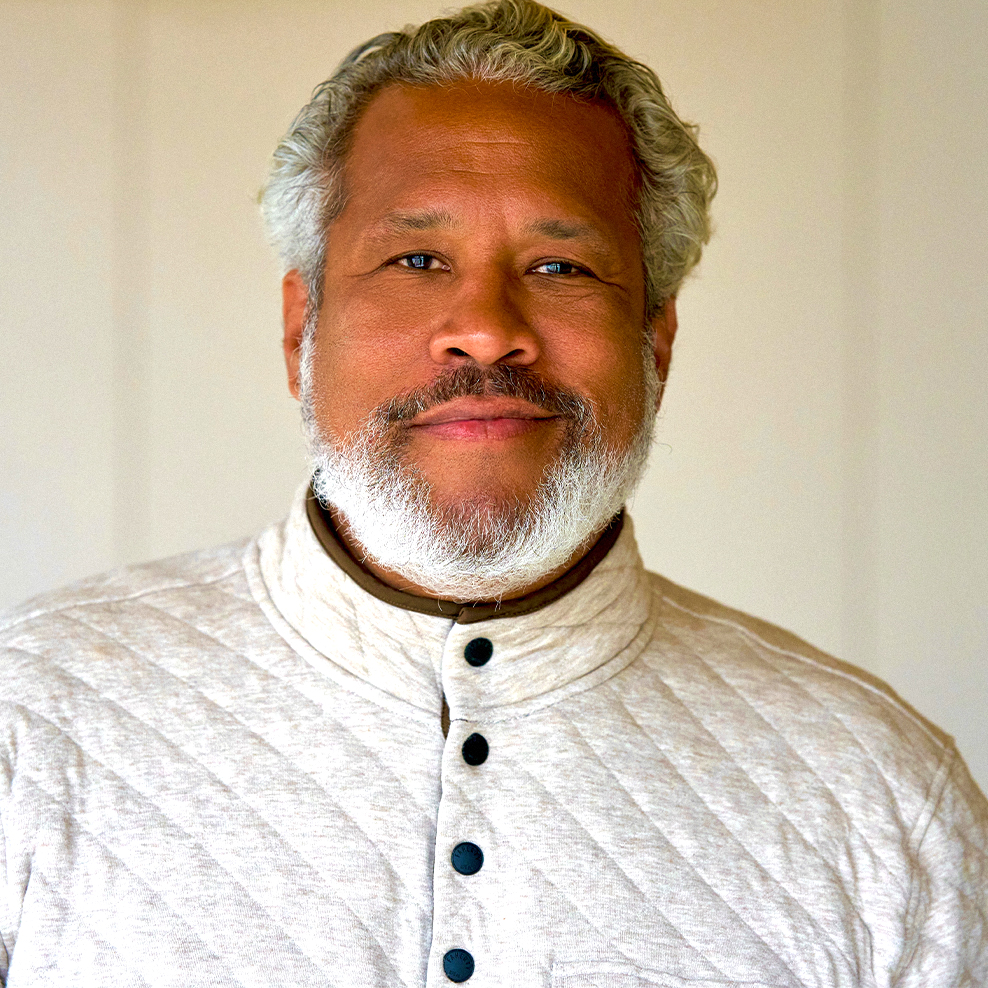 This is a photo of Khary Lazarre-White smiling and wearing a white button-up sweater.