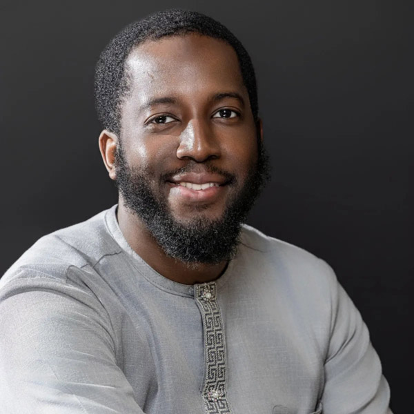 This is a headshot photo of Husein Yatabarry smiling and wearing a light gray button-up shirt.