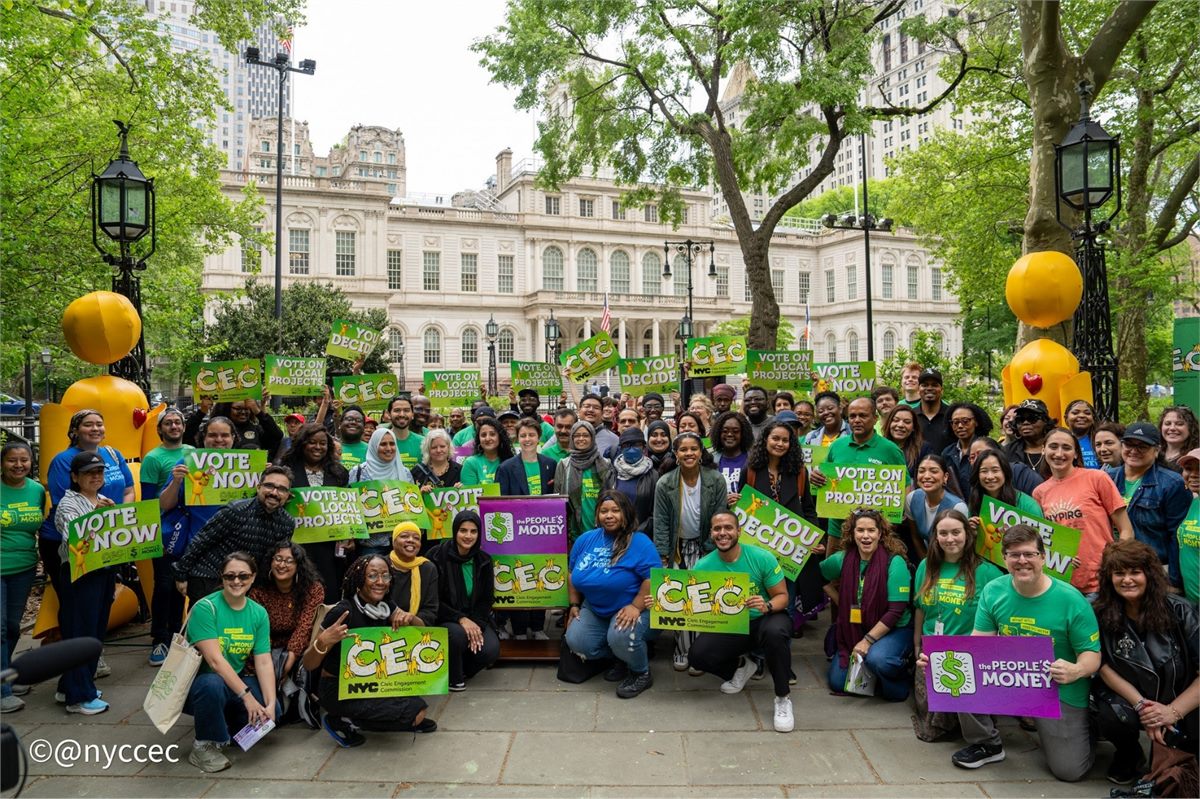 Group photo of about 50 people smiling and holding up CEC and People&rsquo;s Money signs in front of NYC City Hall at the voting launch event