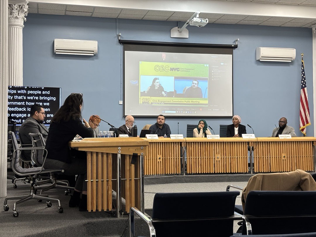 This photo shows Tascha Van Auken presenting to CEC commissioners seated around a table on the stage at Spector Hall.