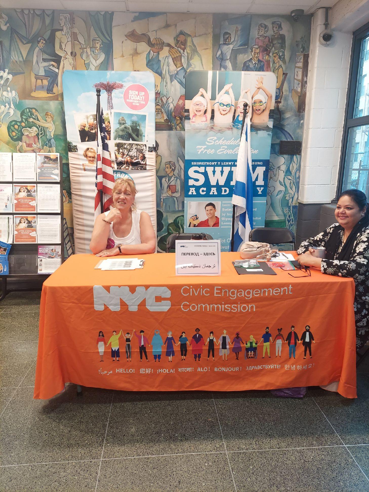 CEC interpreters sitting at table with orange cover that reads NYC Civic Engagement Commission