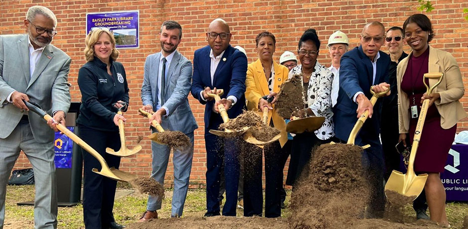 A group of people celebrate a capital project groundbreaking ceremony by shoveling dirt with shelves that have been painted gold
                                           