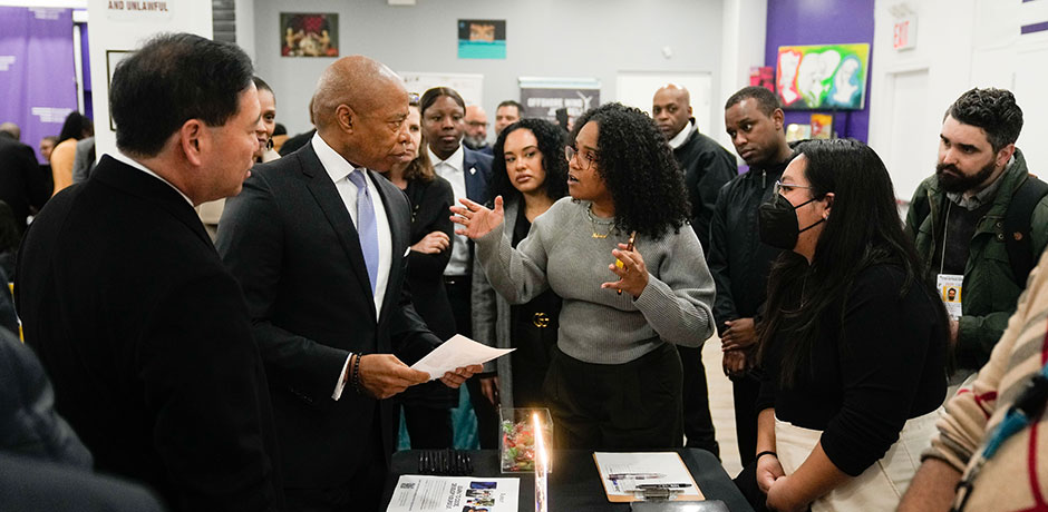 A woman who is tabling is having a conversation with Mayor Adams at a Jobs NYC event. There is also a crowd surrounding them listening in
                                           