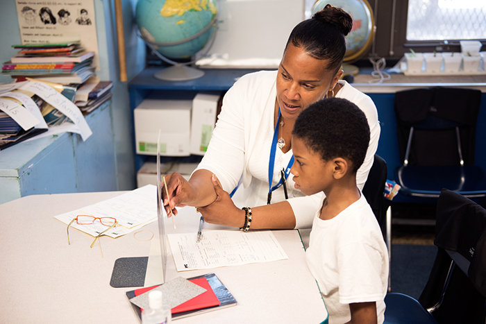 woman sitting at table in classroom conducting eye test on boy in school