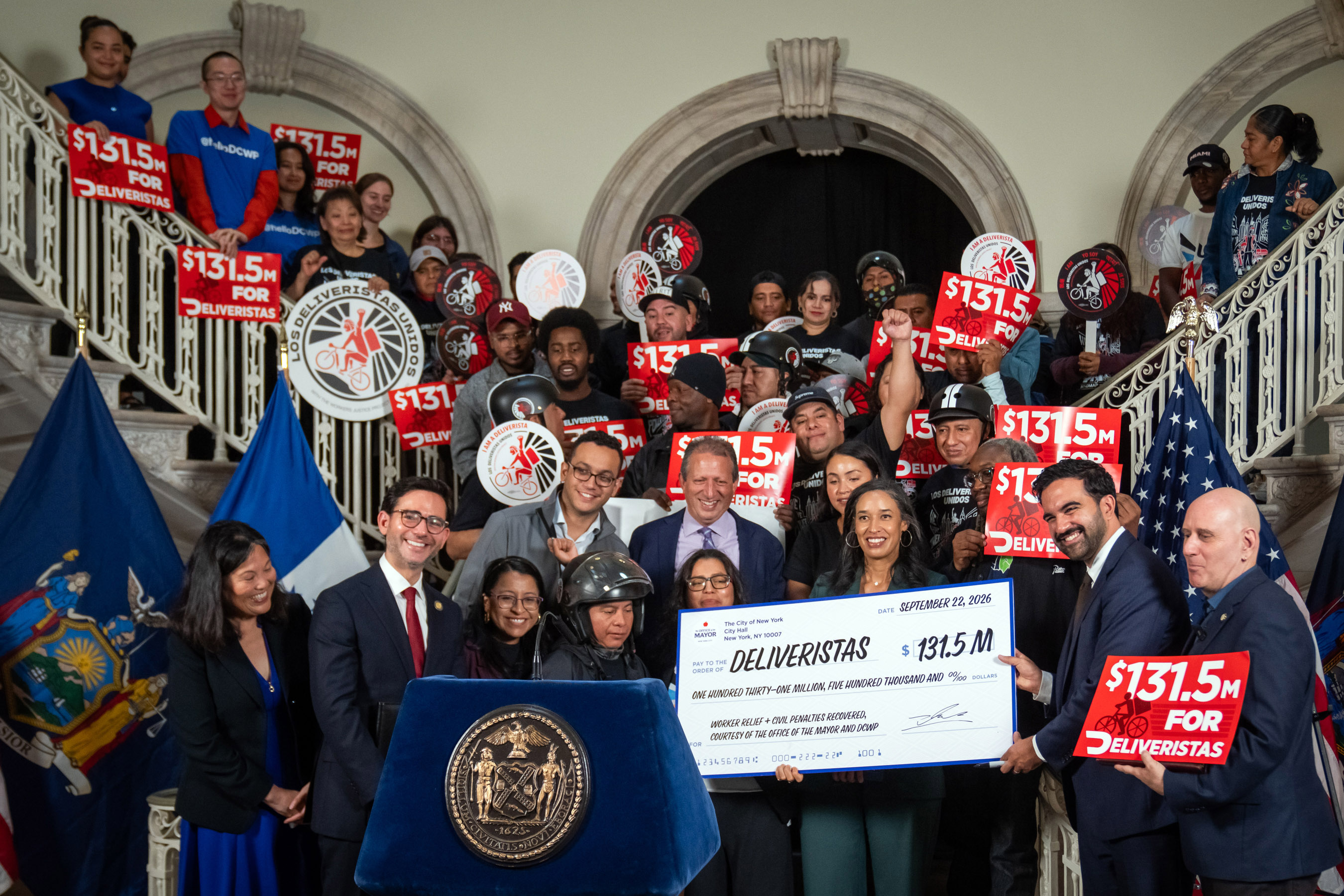Mayor Mamdani, DCWP Commissioner Levine, Julie Su, Brad Lander, and members of Los Deliveristas Unidos pose with $131.5 million check from Doordash
