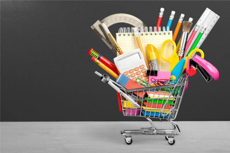 Shopping cart filled with pencils, erasers, scissors, and other back to school supplies.
                                           