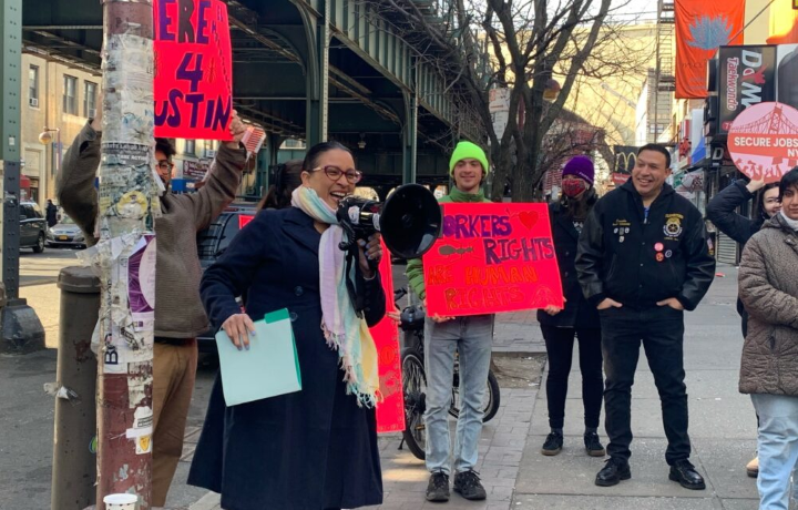 Commissioner Mayuga stands outside with a megaphone and a crowd of New Yorkers holding signs.
                                           
