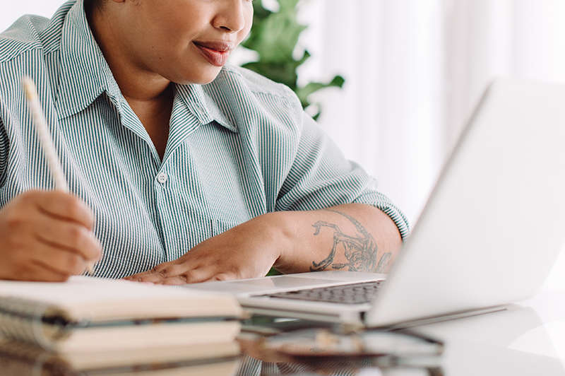 Freelancer writing notes during video meeting on laptop
                                           