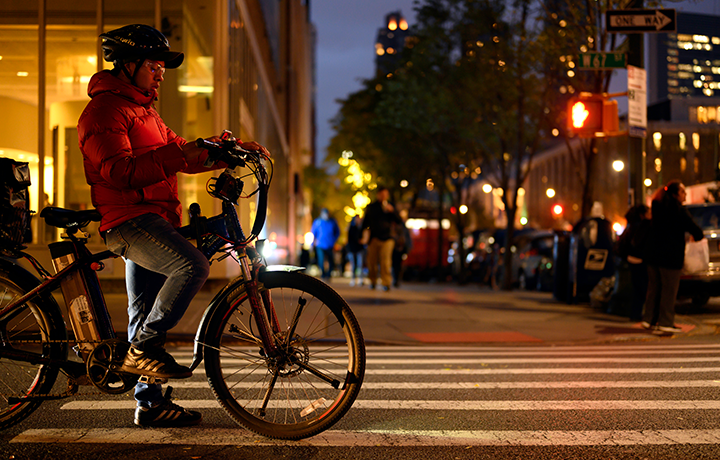 A restaurant delivery man on a bicycle pauses at a stoplight to check his mobile phone on the upper west side of Manhattan on an autumn night

                                           