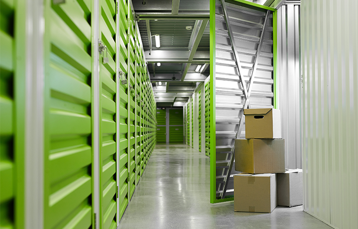 Background image of green self-storage facility with opened unit door and cardboard boxes
                                           