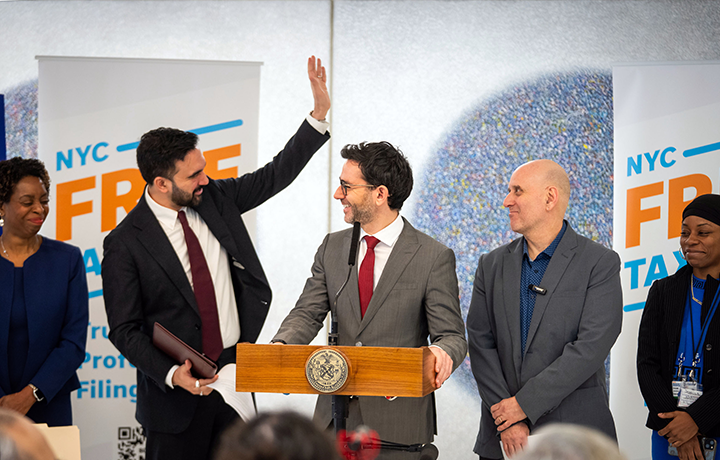 Commissioner Sam Levine stands speaks at podium with Mayor Zohran Mamdani, Council Member Harvey Epstein, and members of NYC Health + Hospitals, MetroPlusHealth, and the NYC Free Tax Prep Volunteer program.
                                           