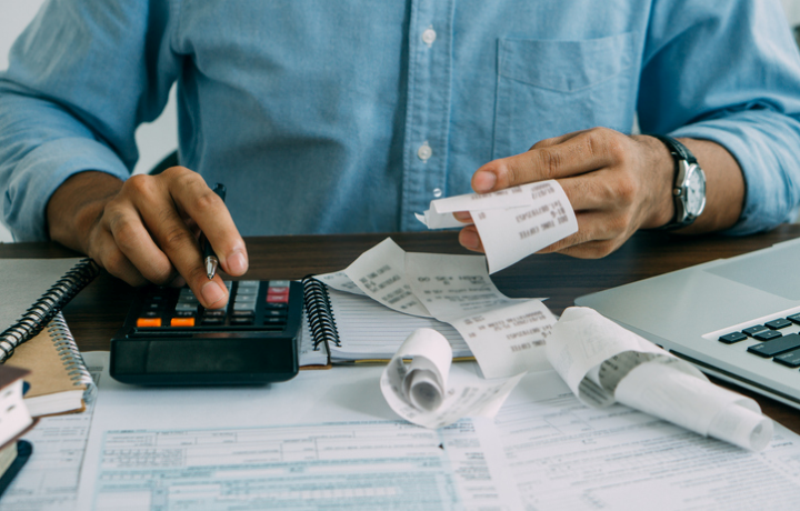 Someone looking over receipts and tax documents with a calculator.
                                           