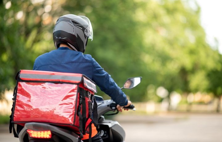 Back of a food delivery worker driving a motorbike on the street.
                                           