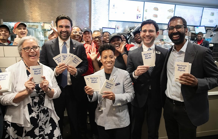 Mayor Zohran Mamdani and Commissioner Sam Levine pose with fast-food workers holding Workers' Bill of Rights
                                           