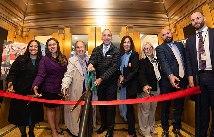 Elected officials gathered in front of gleaming brass doors holding scissors for a ribbon cutting.
                                           