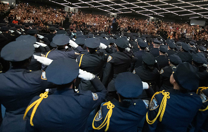 NYPD recruits in an auditorium facing the audience and saluting.
                                           