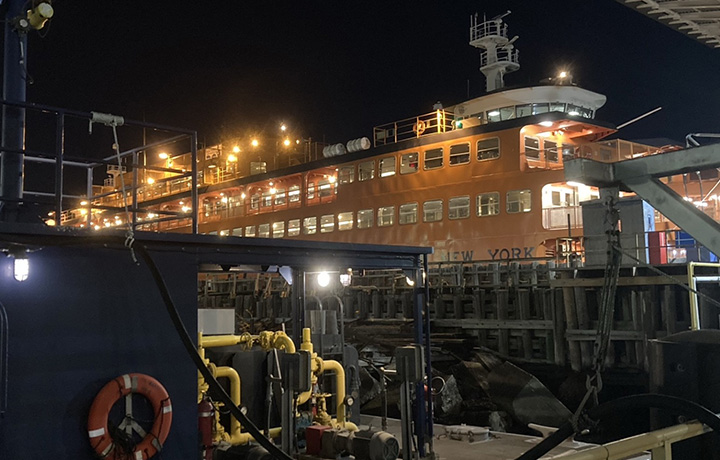 Staten Island Ferry at the dock. All interior lights are on shining bright against the nighttime sky.
                                           