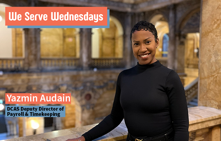 Woman wearing a black shirt and scarf walks through a building with large marble pillars.
                                           