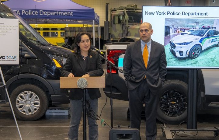 D C A S Commissioner Kitasei and D/C, Fleet Management and Chief Fleet Officer Kerman behind the podium at the 2026 Auto Show making an electric vehicle announcement.
                                           