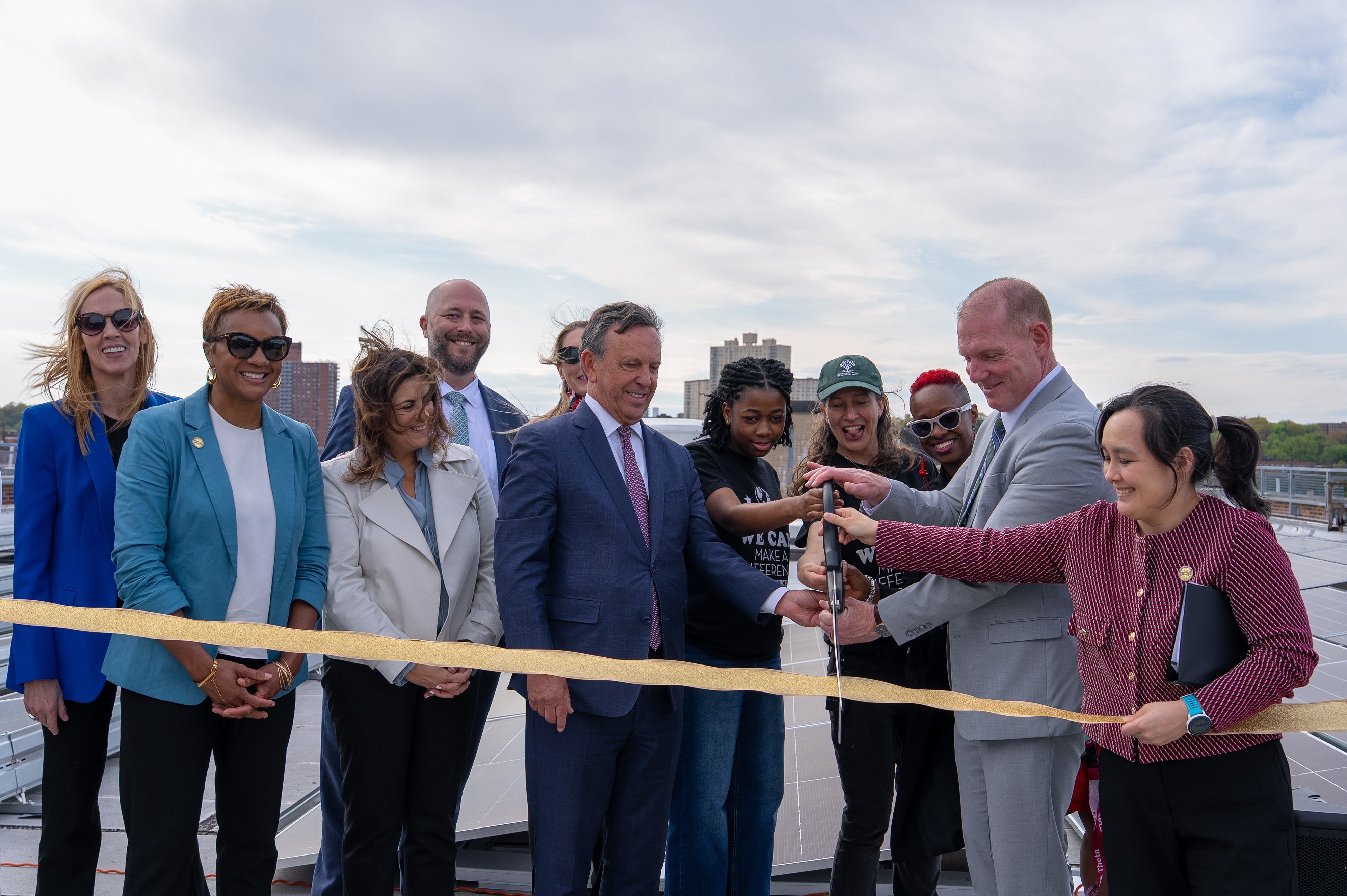 Various city and state officials and NYC Schools students on a rooftop of a school cutting a ribbon. 
                                           