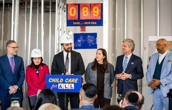 Mayor Mamdani, Commissioner Kitasei wearing hard hats join other city officials at a construction site with a  Days to a New Era countdown at 89 in the background.
                                           