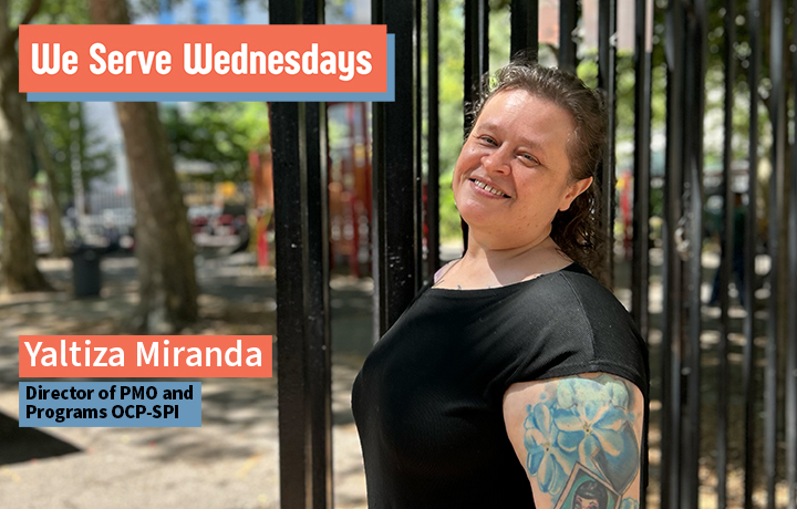 Smiling woman wearing a black tee leaning on a fence.
                                           