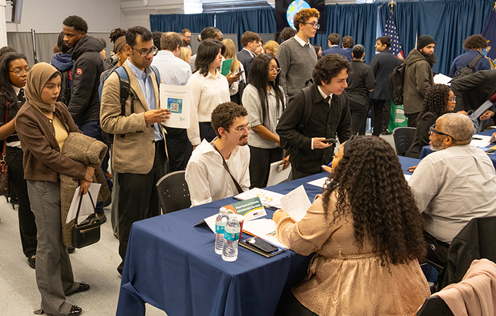 Hiring fair with candidates standing on line and interviewed at the tables with hiring professionals