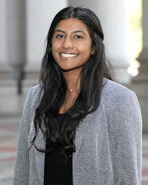 Vaishnavi is standing outside, smiling, wearing a black shirt and grey blazer.