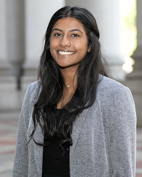 Vaishnavi is standing outside, smiling, wearing a black shirt and grey blazer.