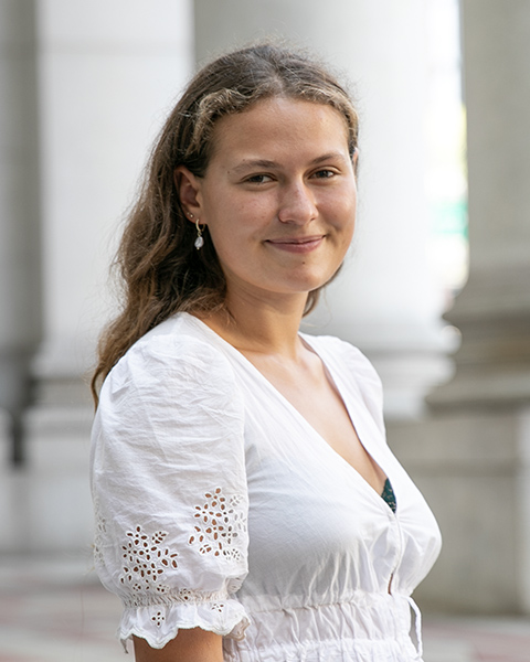 Sophie with long blonde hair is smiling, is wearing a white shirt.