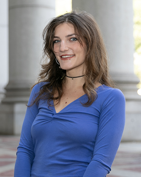 Jacqueline is standing outside, smiling, wearing a blue shirt.