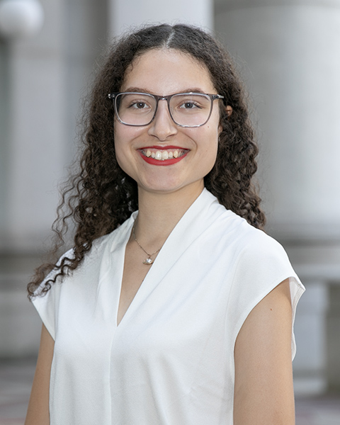 Yvonne is standing outside, smiling, is wearing glasses and a white shirt.