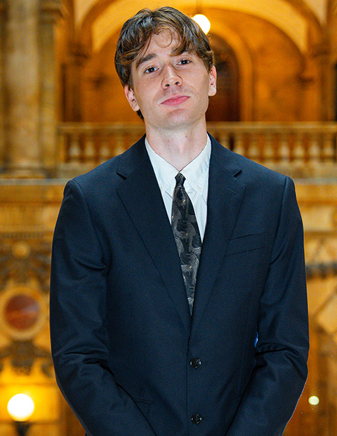 Person smiling, wearing a navy blazer, white shirt and tie.