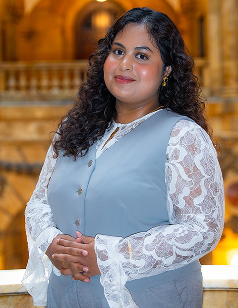 Person smiling, wearing a light blue vest and white lace shirt.