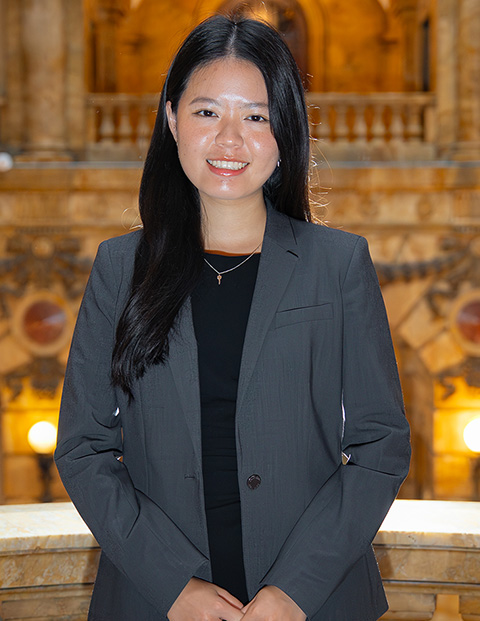 Person smiling, wearing a black dress and grey blazer.