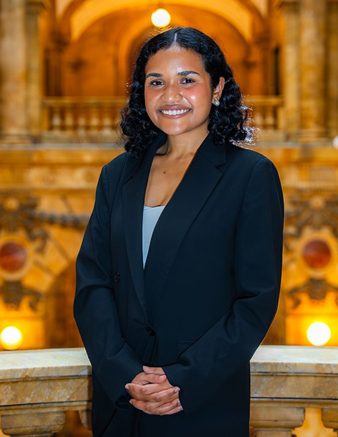 Person smiling, wearing a dark blazer and blue shirt.