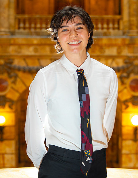 Person smiling, wearing a white shirt, black pants and tie.