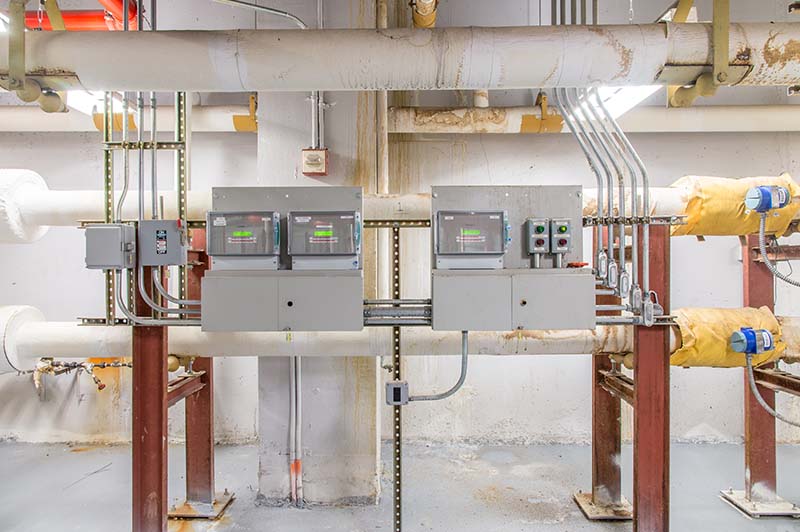 Three real time meters measuring electricity use in a boiler room of a public building.
