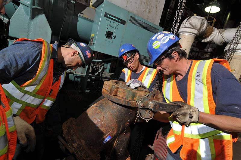 Three city staff installing a Y-strainer as part of a capital HVAC system upgrade.