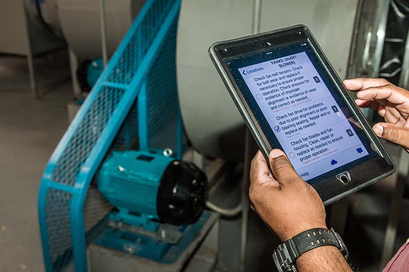 An individual with a tablet stands in front of a fan motor auditing the blowers performance. 