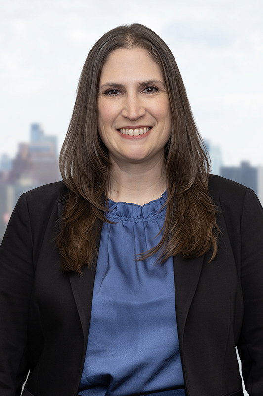 Smiling woman wearing a dark suit in front of the Brooklyn skyline