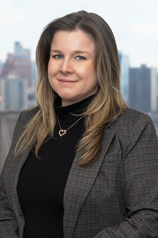 Woman smiling wearing a dark suit poses with the Brooklyn skyline in the background.