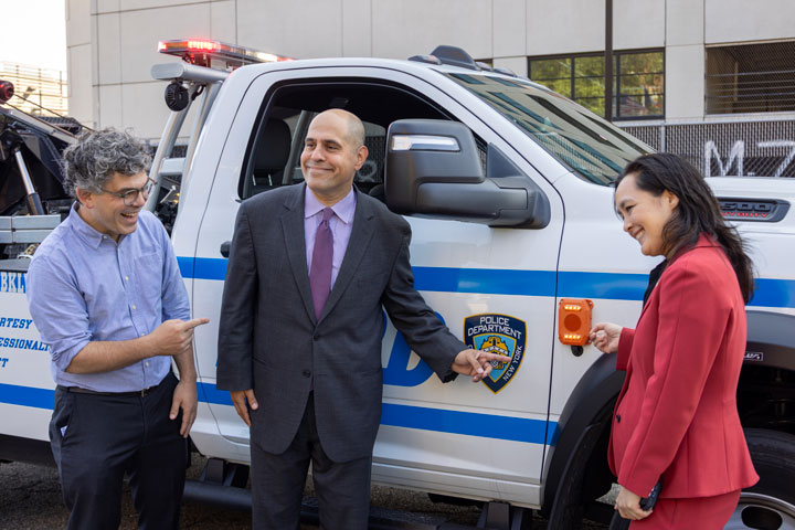 Council Member Lincoln Restler, DCAS Deputy Commissioner and NYC Chief Fleet Officer Keith Kerman, and DCAS Commissioner Yume Kitasei pose with an NYPD vehicle featuring pedestrian alerts.
                                           