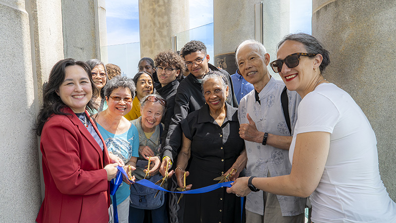 A group of experience participants and city officials smile while holding scissors during a blue ribbon-cutting ceremony inside Centre 360, surrounded by stone columns and glass panels.